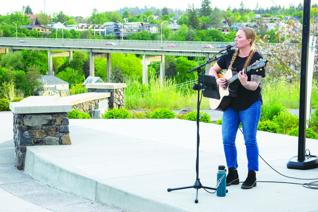 Artist Jessica Haffner performing her set list with a backdrop of the Spokane River 